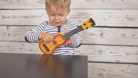 One year old boy plays his guitar or ukulele and sings songs, sitting in the Video stock 97246941
