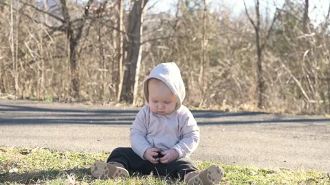 One year old  boy sits on the grass and explores nature, in the park, early s Stock Footage 270461286
