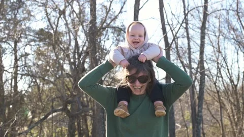 One year old boy sits on his mother's shoulder and playing, spring, trees, in Stockbeeldmateriaal 270461341