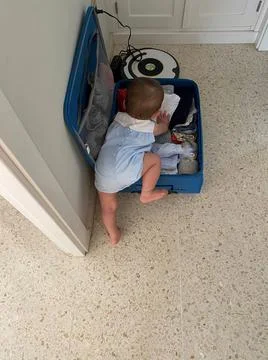 One-year-old boy stuffing himself into a suitcase full of clothes in a hall Stock Photos