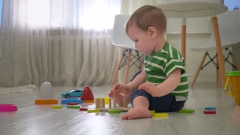 A one-year-old child is deeply engrossed in the process of assembling a wooden t Stock Footage 300878258