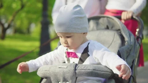 A one-year-old child drives in a stroller with parents in the park. Slow motion Stock Footage 76101100