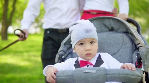 A one-year-old child drives in a stroller with parents in the park. Slow motion 库存影片 76101369