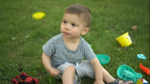 A one-year-old child sits on the grass and plays with toys. Little boy in the Stock-Footage 247000210