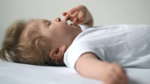 One year old disabled boy in white bodysuit is lying on his back and yawning Stock Footage 101794355