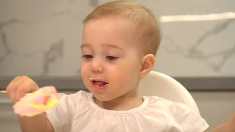 One-year-old girl eats meringue in the kitchen Stock Footage 128776845