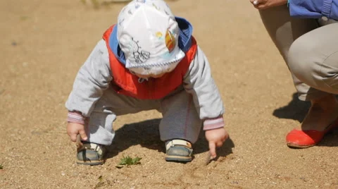 One year old kid playing with sand on the playground. Near the mother helps him Stock Footage 66463645