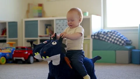 One year old red-haired boy, sitting on a toy and laughing,  in the children' Stock Footage 270198867