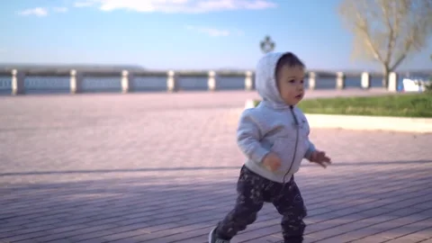 A one-year-old son runs along the paving stones on the embankment. A small child Stock Footage 243354609