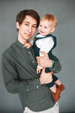 A one-year-old son sits in the arms of a young father Stock Photos