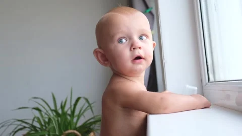 A one-year-old toddler boy plays and toys while standing near the window and Stock Footage 250077286
