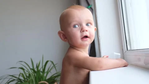 A one-year-old toddler boy plays and toys while standing near the window and Stock Footage 254040377