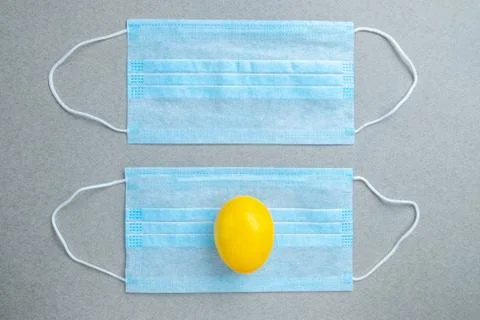 One yellow easter egg lies on a blue medical mask on a gray background. Stock Photos