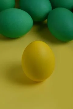 One yellow painted Easter egg stands in front of green eggs. Stock Photos