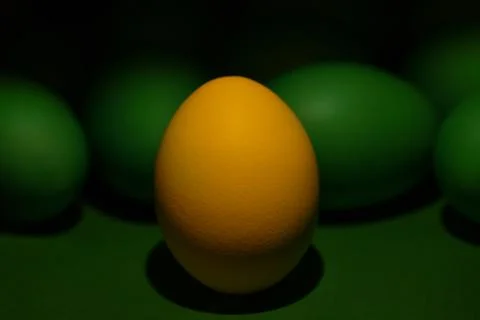 One yellow painted Easter egg stands in front of green eggs on a green Фото