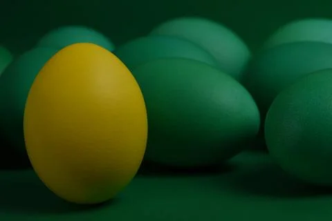 One yellow painted Easter egg stands in front of green eggs on a green Fotos de archivo