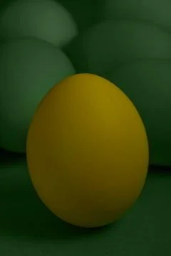 One yellow painted Easter egg stands in front of green eggs on a green Stock Photos