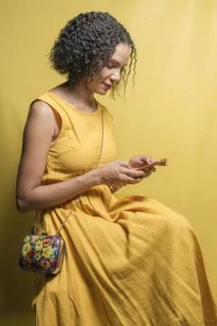 One young adult brunette woman wearing long yellow dress using smartphone Stock Photos