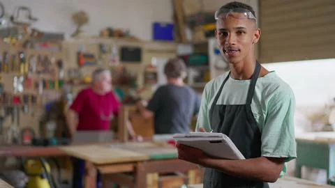 One young black apprentice of carpentry workshop taking notes on notepad, w.. Foto stock