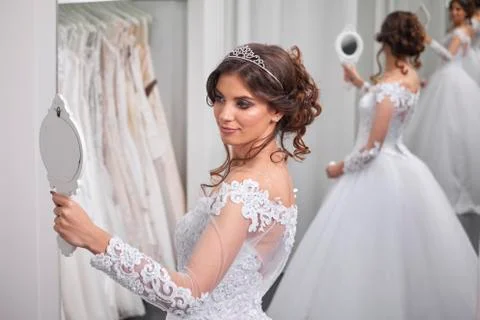 One young bride, looking at self in mirror, bridal salon, wearing gown. Stock Photos