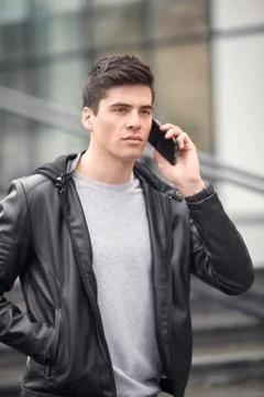 One young handsome man posing outdoors, wearing jacket, talking over smartpho Stock Photos
