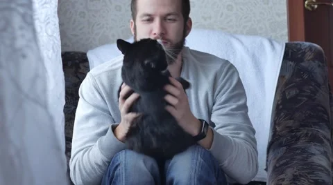 One young man with a beard playing with her black cat Stock Footage 68753151