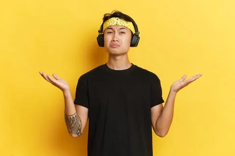 One young man in black T-shirt posing isolated on studio yellow background, he's Stock-Fotos