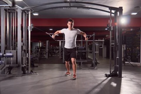 One young man, Multi-Station Gym Machine cable pull exercise, dark gym indoor Stock Photos
