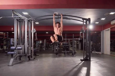 One young man, Multi-Station Gym Machine abs exercise, dark gym indoors, full Stock Photos