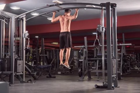 One young man, Multi-Station Gym Machine, back exercise, rear view, dark gym  Stock Photos
