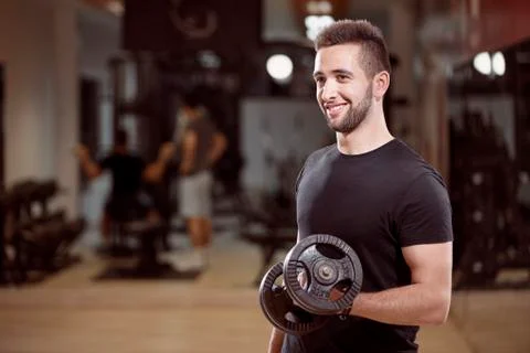 One young man, ordinary average looking, one arm dumbell exercise, smiling, i Stock Photos