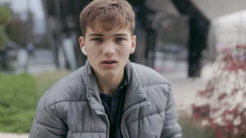 One young man putting earphone and looking at camera outdoor in urban style. Video stock 332765822