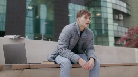 One young man sitting on bench thinking near modern glass corporate building. Stock Footage 332766105