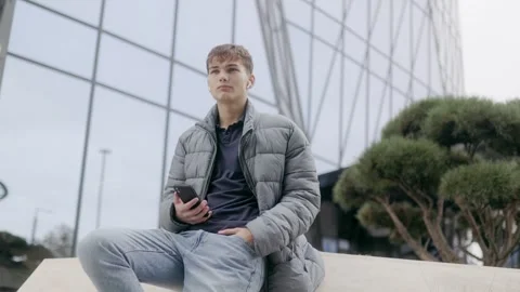One young man sitting with phone and thinking outdoor in cinematic style. Stock Footage 332765833