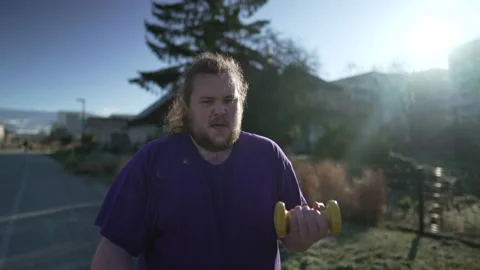 One young overweight man working out lifting dumbbells outside. A fat chubb.. Stock Footage 232722864