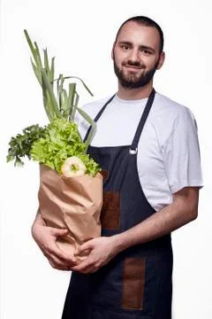 One young smiling chef posing, studio shot, white background, holding groceri Stock Photos