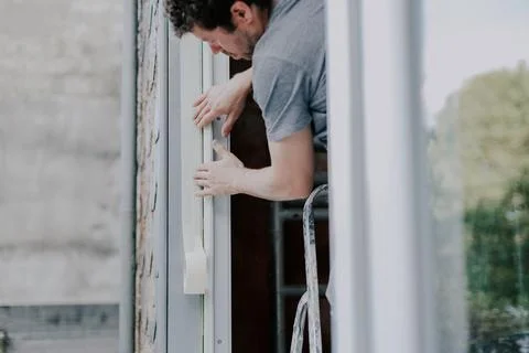 One young worker repairs window frames by gluing on tape. Stock Photos