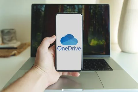Onedrive cloud storage application logo on smartphone screen in front of laptop Stock Photos