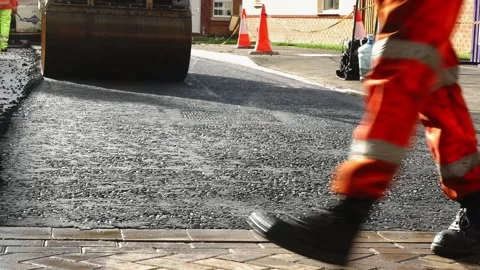 Ongoing road contruction with roller machine and worker walking across Stock Footage 233000705