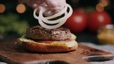 Onion Being Placed On Hamburger Bun With Lettuce And Tomato Video stock 134410480