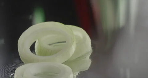 Onion rings fall on a mirror area with water Stock Footage 198345632