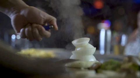 Onion volcano getting lit by Teppanyaki chef during dining experience, Stock Footage 130165566