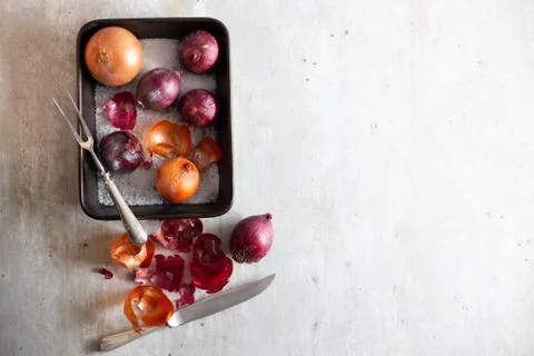 Onions in a baking sheet on a gray surface with kitchen utensils Stock Photos