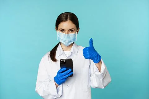 Online doctor and clinic. Young woman in medical face mask, using smartphone for Stock Photos