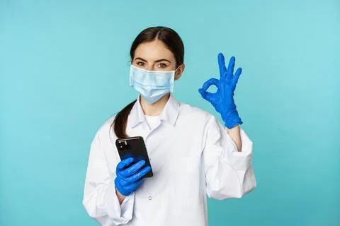 Online doctor and clinic. Young woman in medical face mask, using smartphone for Stock Photos