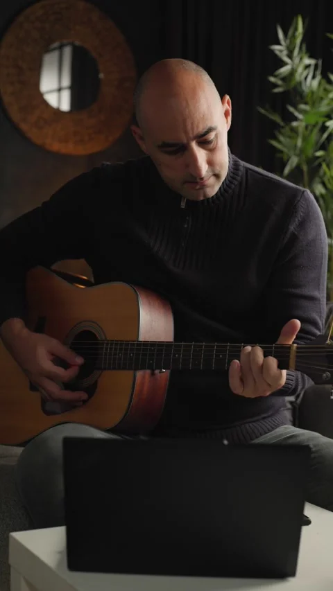 Online music lesson concept, man playing acoustic guitar while watching Stock Footage 344144053