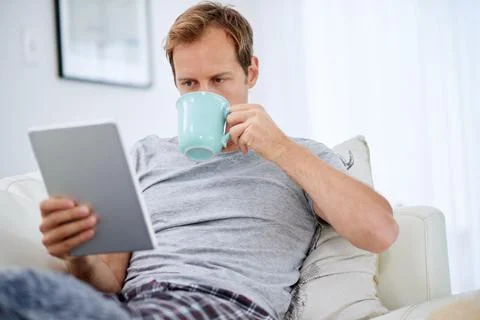 Online news and a cup of java. a handsome man drinking coffee while using his Stock Photos