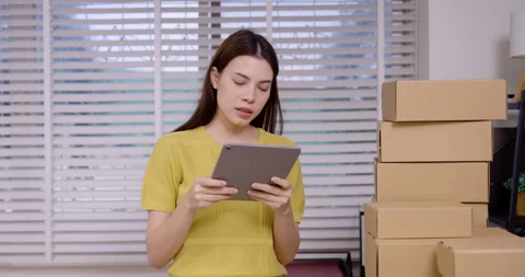 Online seller holding tablet while inspecting stacked parcel boxes, checking Vidéo 330841980