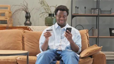 Online Shopping  by African Man while Sitting on Sofa at Home Video stock 299761553