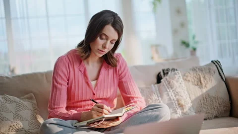 Online student making notes watching laptop educational video in home closeup. Stock Footage 332817835